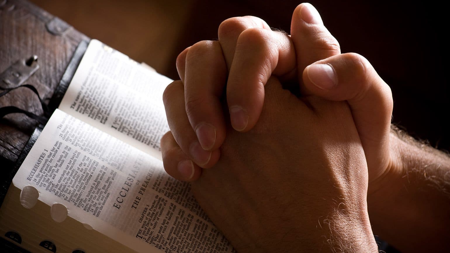 Hands clasped in prayer over an open Bible